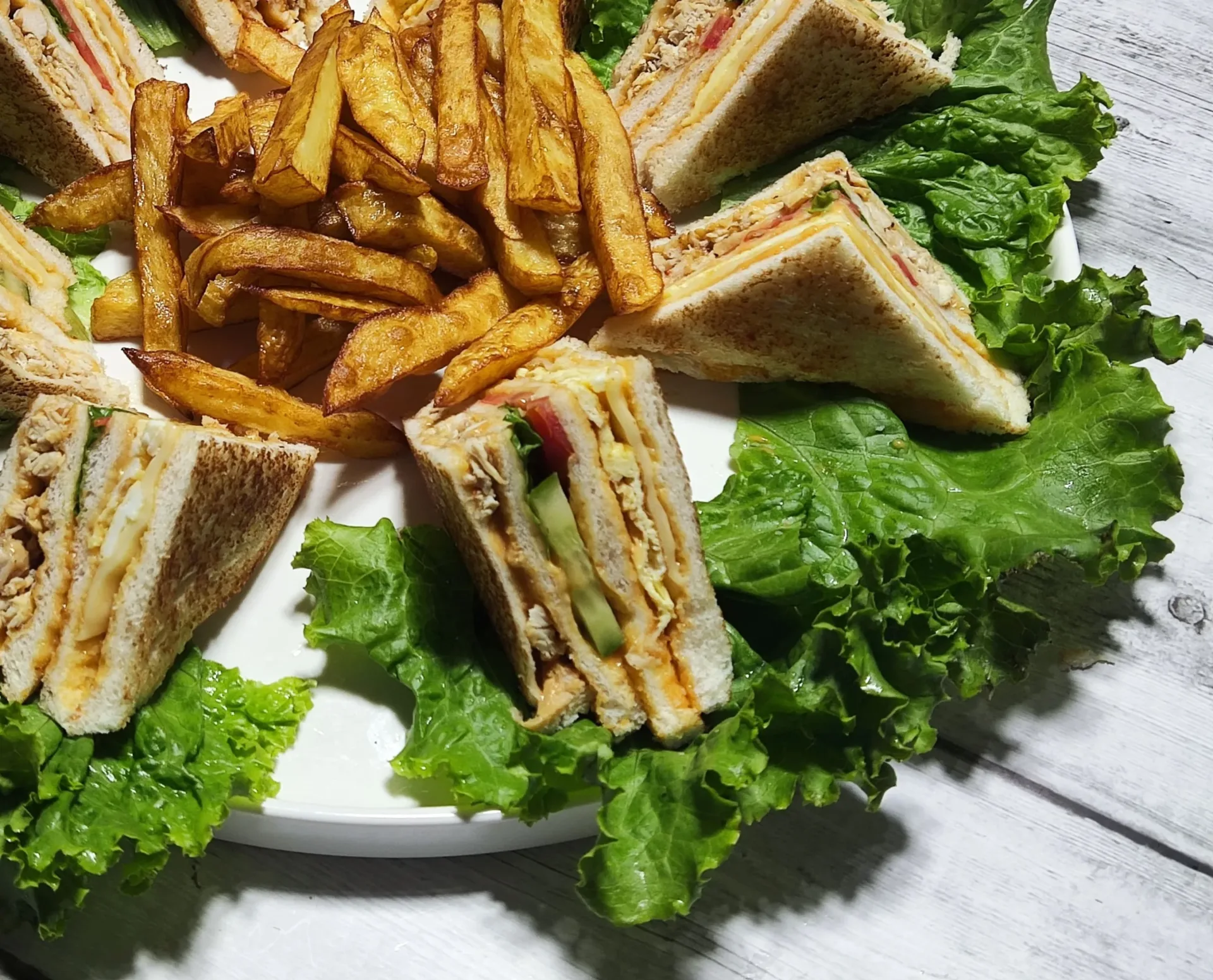 close shot of chicken club sandwich served in plate with lettuce and fries