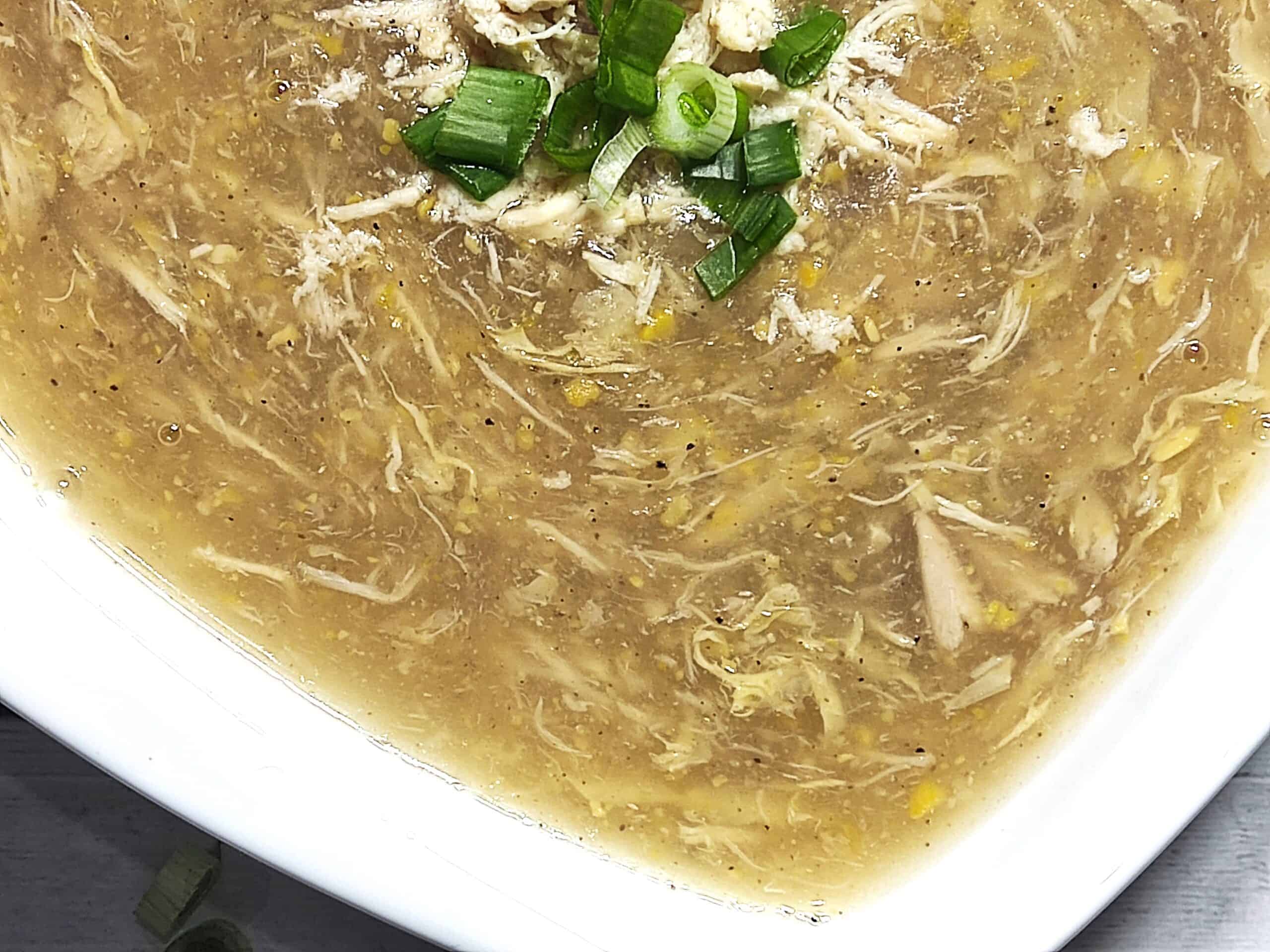 a close shot of chicken corn soup served in white bowl with sprinkle of spring onion on top of soup
