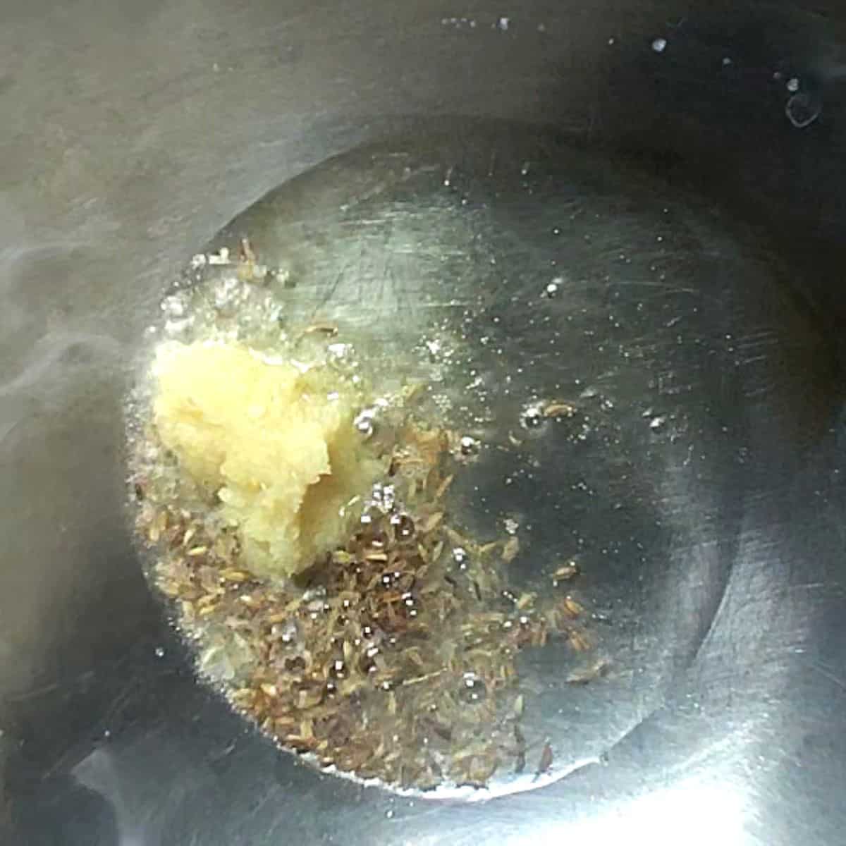 silver wok showing ginger garlic pase is add with oil and zeera