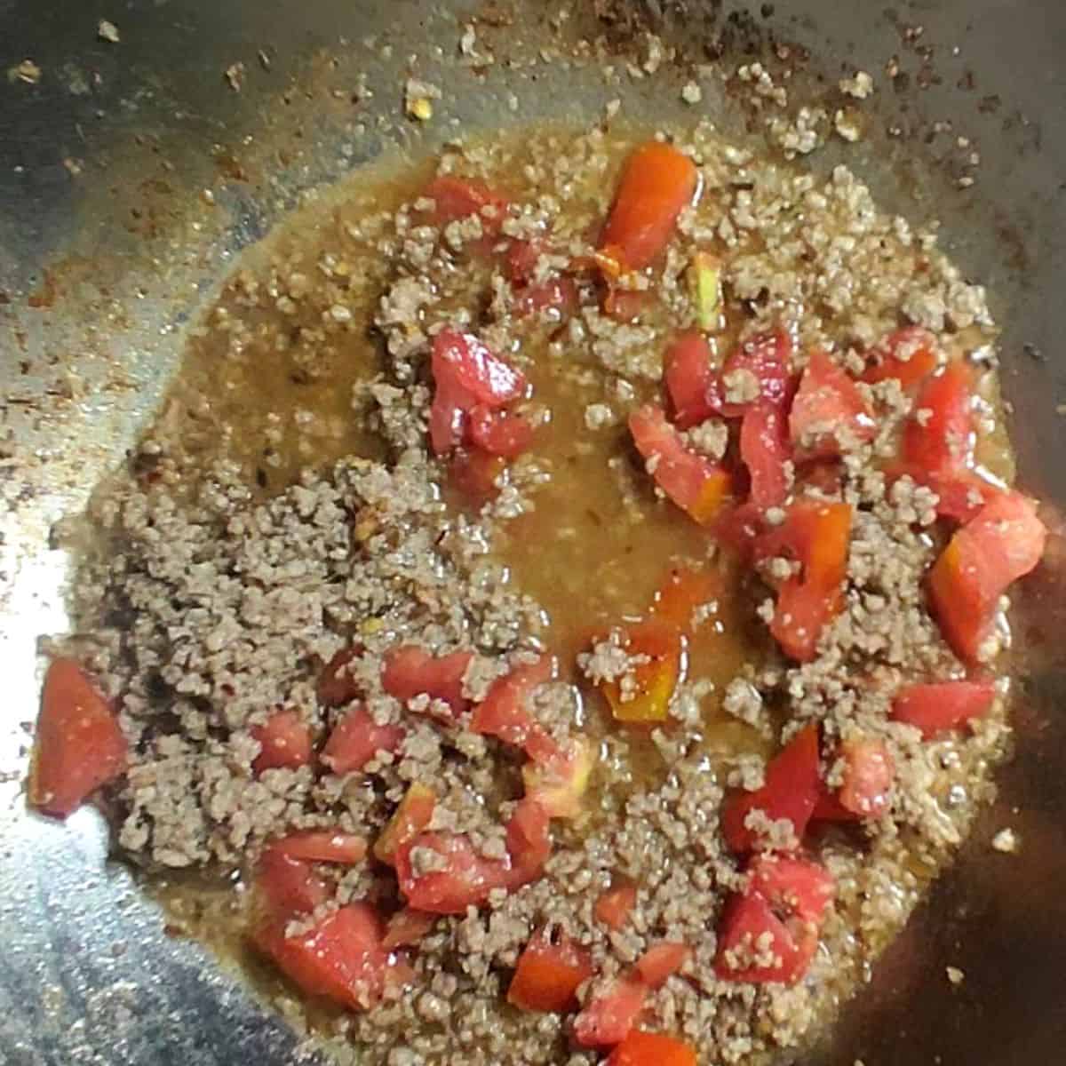 silver wok containing beef mince with fresh tomatoes 
