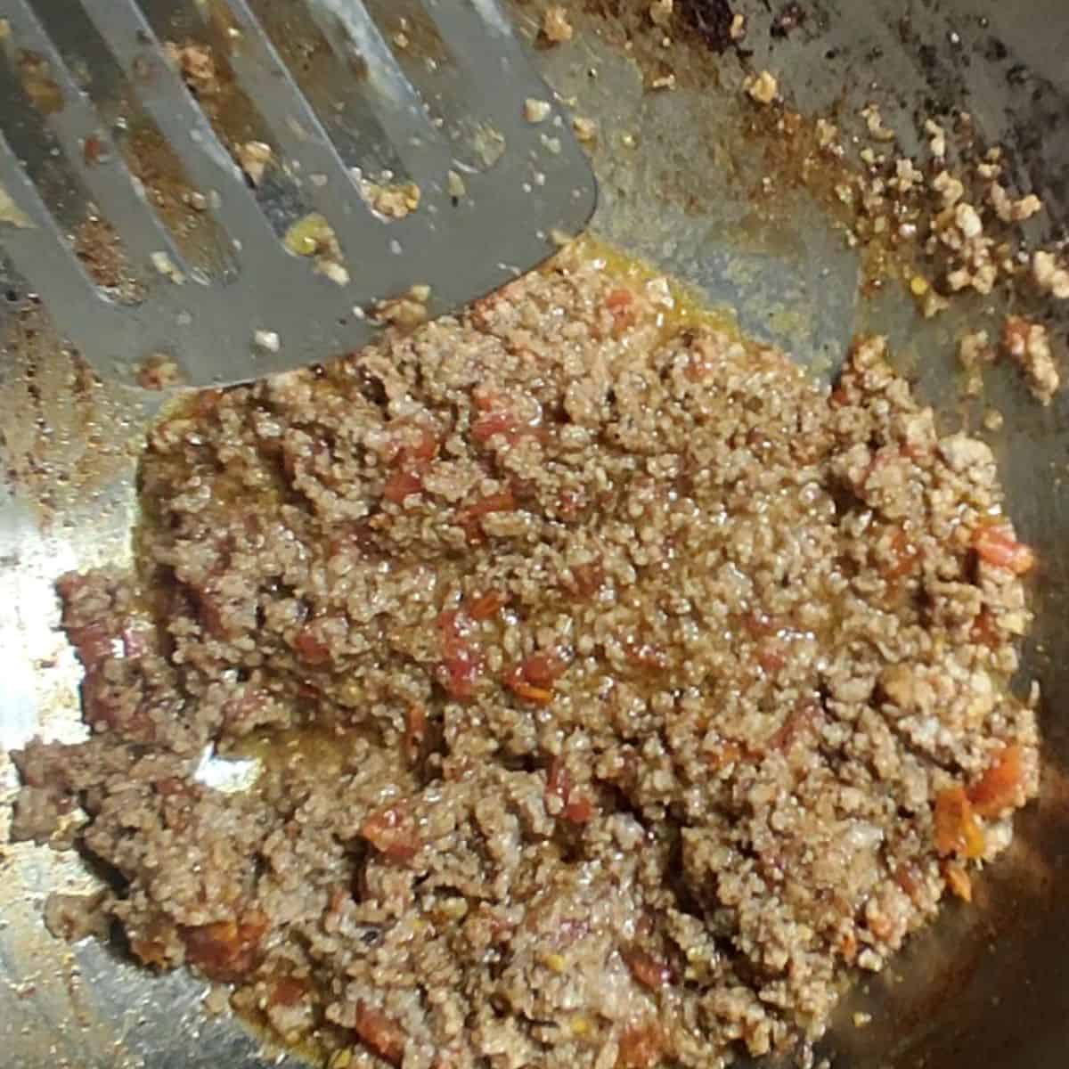 a hand with a spoon mixing beef mince in silver wok