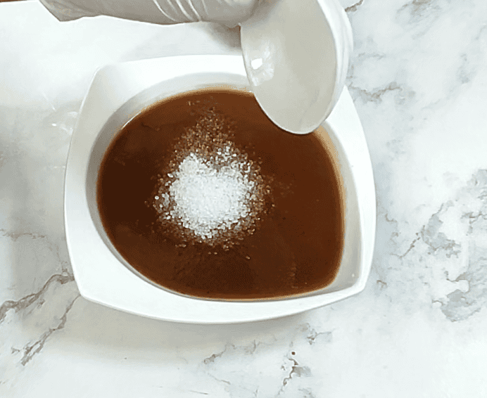 Tamarind chutney in white bowl with powdered sugar garnish on marble surface.