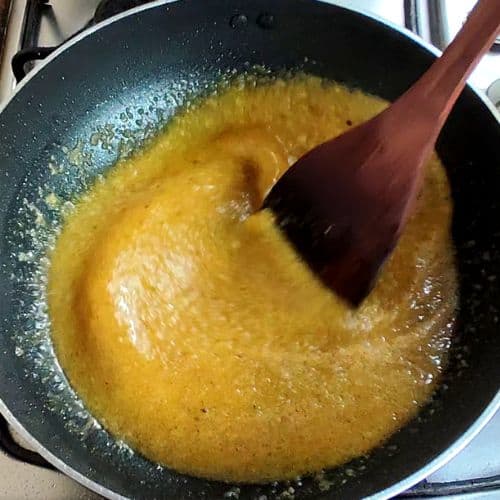 Golden curry paste being stirred in a wok with a wooden spatula during fish curry preparation.