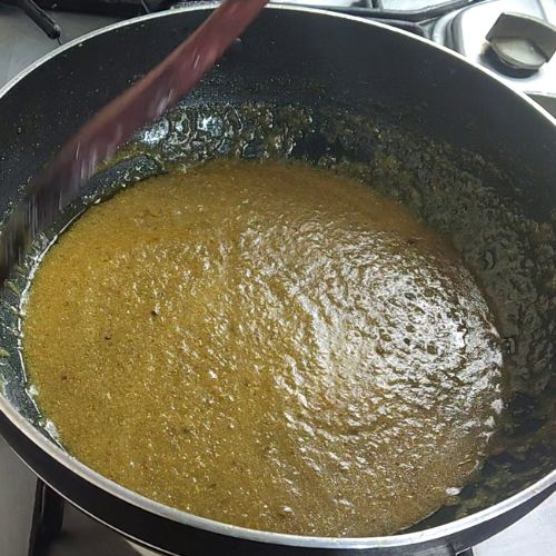Simmering fish curry base with golden-brown gravy in a large black pot with wooden spoon.