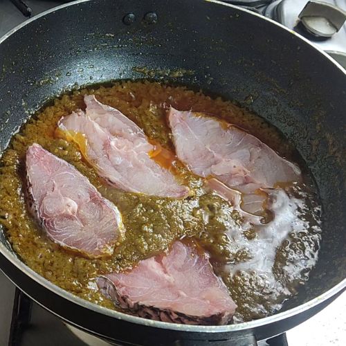 Fish curry in a dark wok with four pink fish fillets simmering in golden-brown sauce.