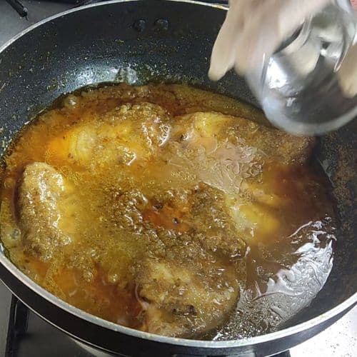 Fish curry simmering in a dark wok with golden-brown broth and tender fish pieces.