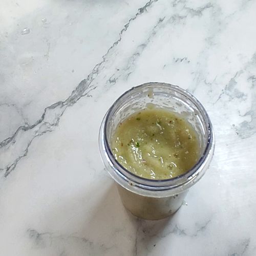 Homemade fish curry paste in glass jar on marble countertop, yellow-green textured consistency.