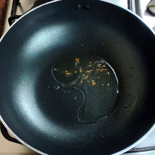 Garlic and spices tempering in hot oil in a dark wok pan for fish curry preparation.