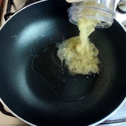 Ginger-garlic paste being poured into a dark wok for fish curry preparation.