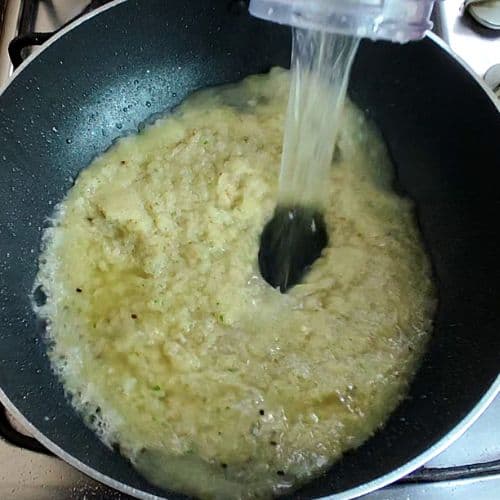 Water being poured into a curry paste cooking in a dark wok, creating a light yellow sauce.