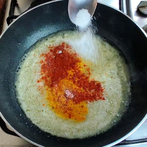 Spices being added to a creamy base in a wok for fish curry preparation.