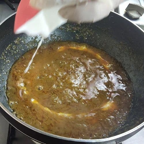 Fish curry simmering in a dark pan with golden-brown sauce and visible ingredients.