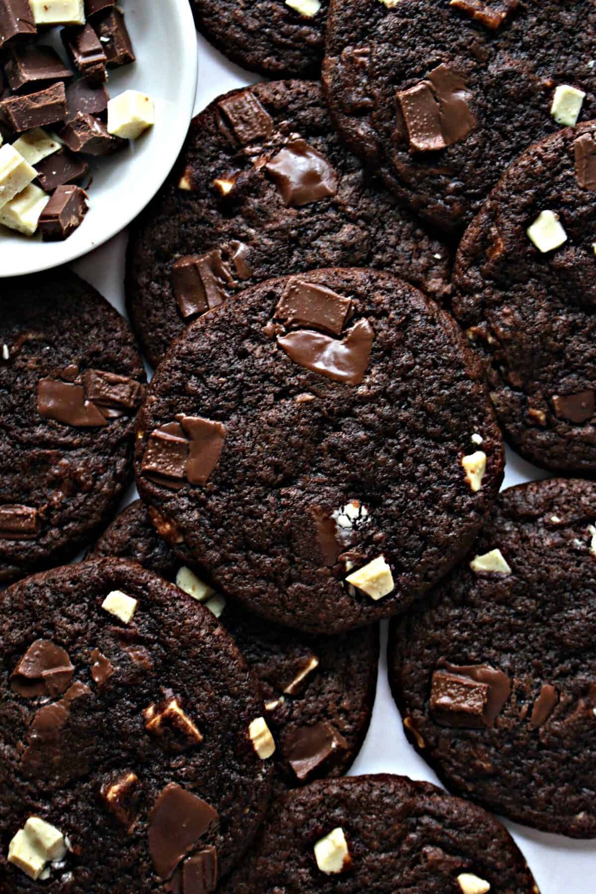 Fudgy chocolate cookies studded with dark and white chocolate chunks arranged on white parchment.