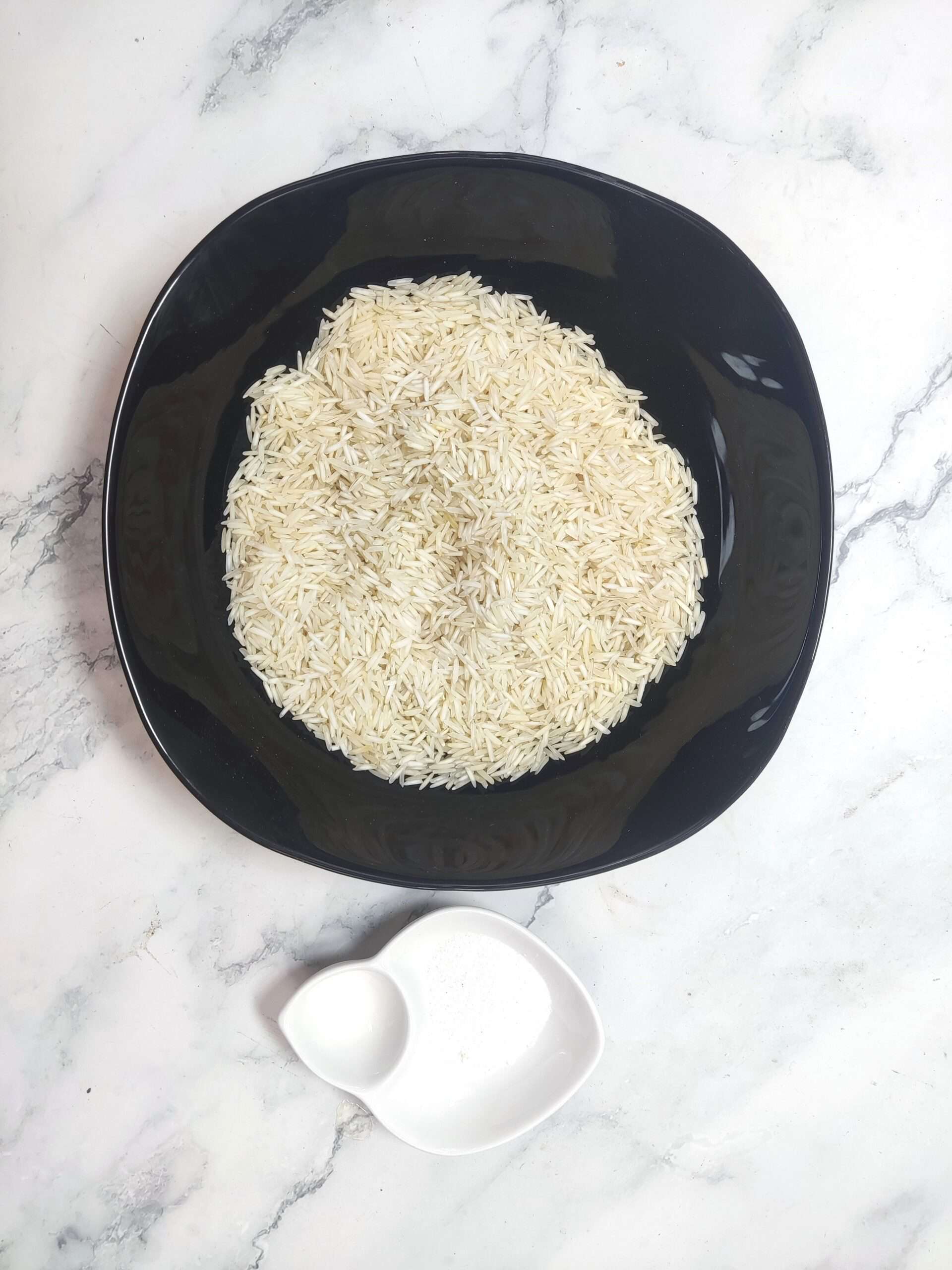 Uncooked basmati rice in black bowl with two eggs in white dish on marble surface.