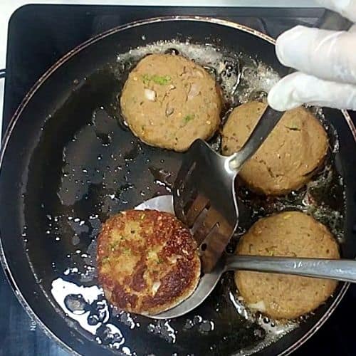 Shami kebabs frying in oil in a dark pan, golden-brown patties with visible herbs and spices.