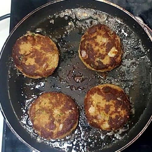 Four golden-brown shami kebabs frying in oil on a dark skillet.