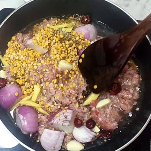 Ground meat and lentils cooking in black pan with onions, corn, and spices for Shami Kebab.