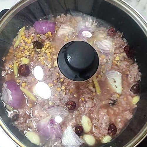 Shami Kebab mixture cooking in pressure cooker with lentils, meat, onions, and spices visible.