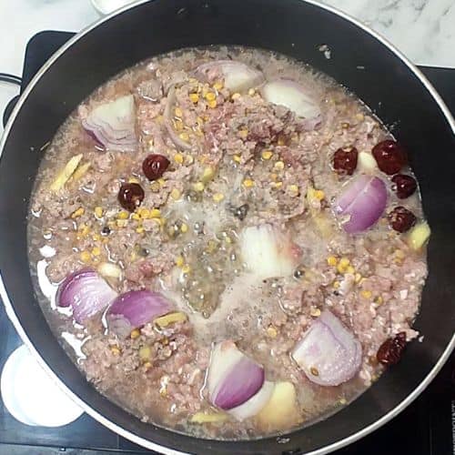 Ground meat mixture with onions, corn, and red chilies simmering in black pot for Shami Kebab.
