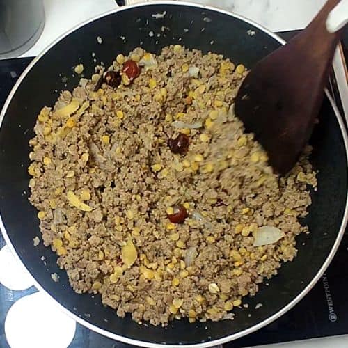 Ground meat mixture with corn and spices being stirred in a black pan for Shami Kebab preparation.