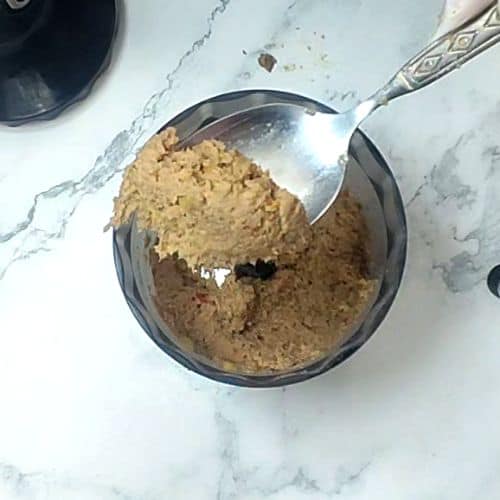 Ground shami kebab mixture in dark bowl with spoon on marble countertop.
