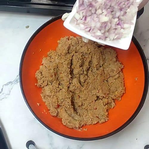 Shami kebab mixture in orange bowl with diced onions in white plate nearby.