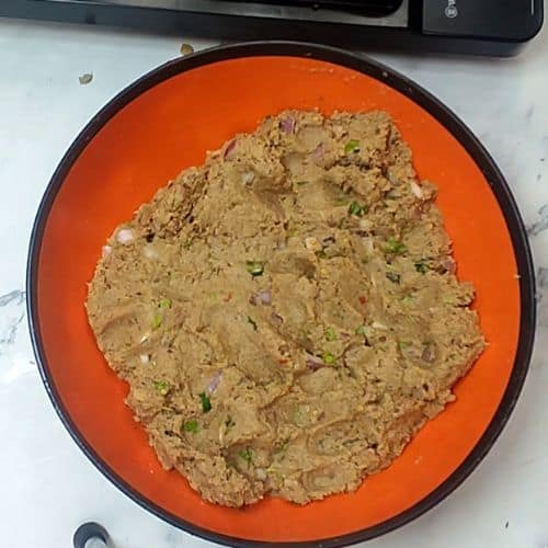 Raw shami kebab mixture on orange plate, showing minced meat texture with herbs and spices.