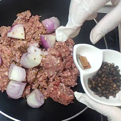 Shami kebab preparation with minced meat, diced red onions, and spices in white bowls on black plate.