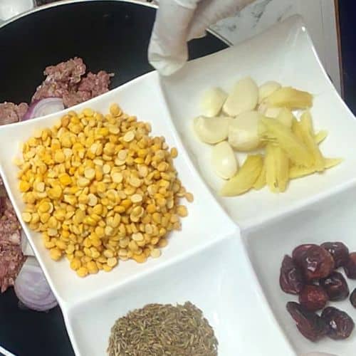 Ingredients for Shami Kebab arranged in white bowls: corn, potatoes, cumin seeds, beets, and ground meat in a pan.