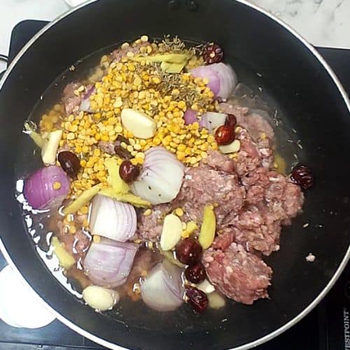 Ground meat, corn, kidney beans, and sliced onions cooking together in a black pan for Shami Kebab.