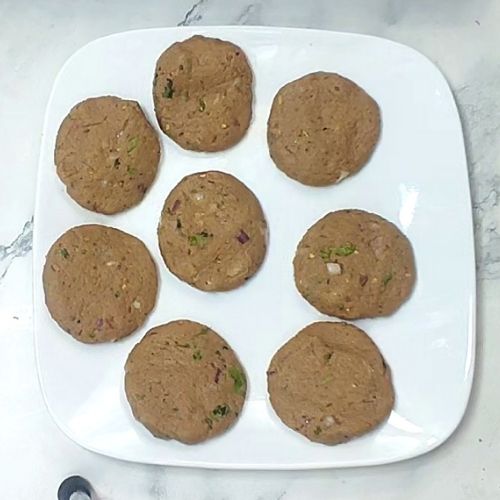 Eight brown shami kebabs with visible herbs arranged on a white square plate.