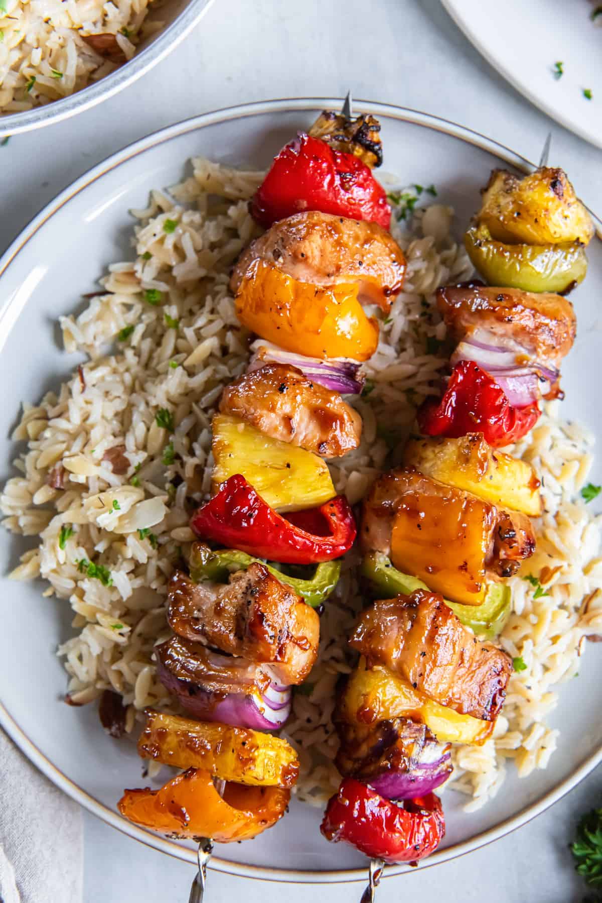 Grilled chicken kabobs with colorful peppers and onions served over herbed rice on white plate.