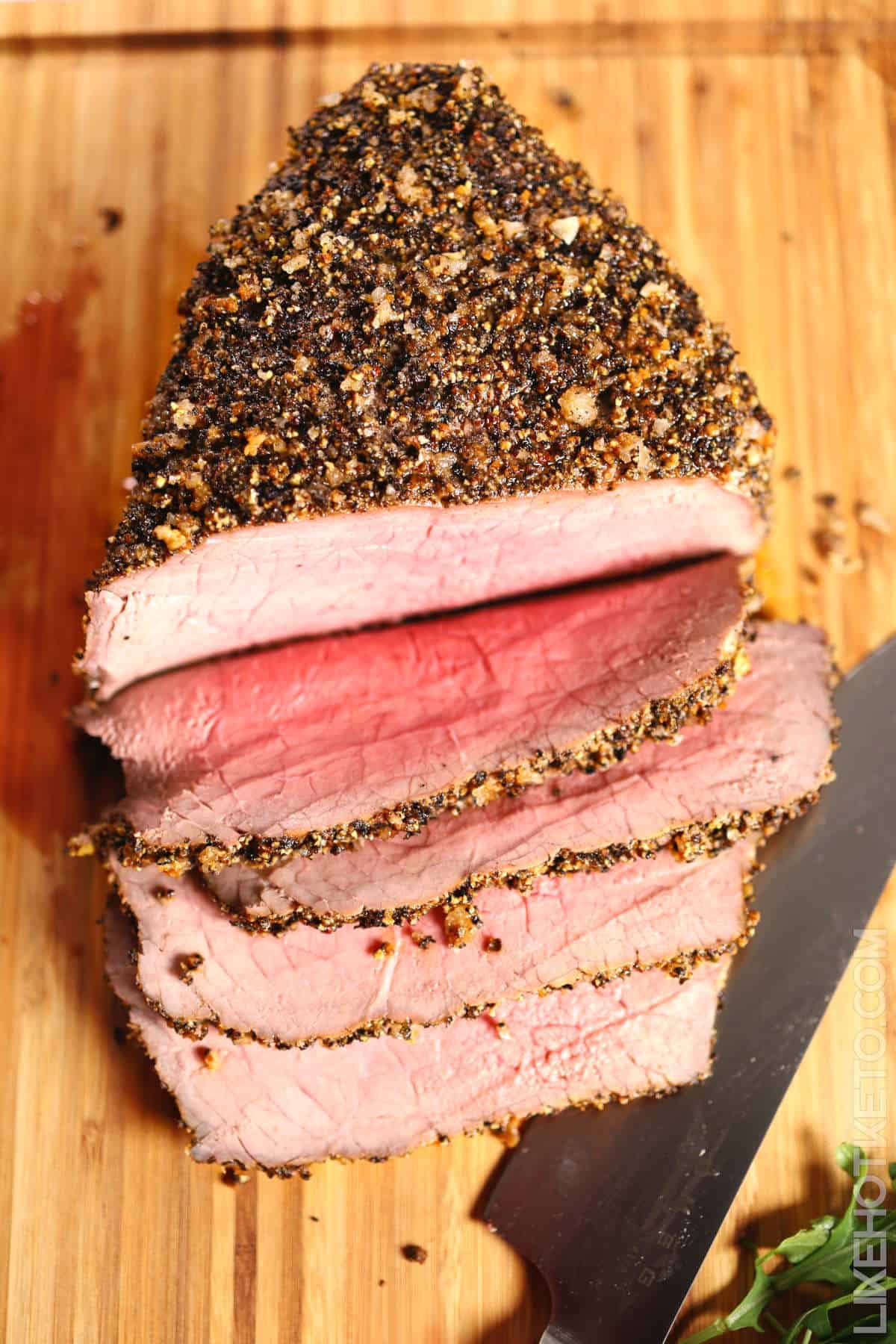 Sliced herb-crusted beef tenderloin with pink center on wooden cutting board.