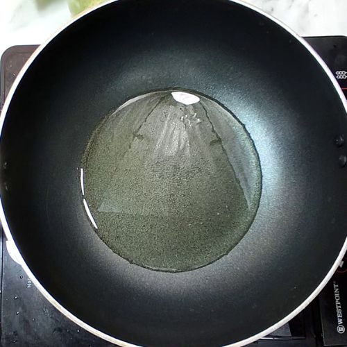 Oil heating in black wok for Pakistani daal mash preparation on stovetop.