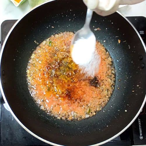 Daal mash cooking in a black wok with cream being stirred in, showing golden-brown lentils.