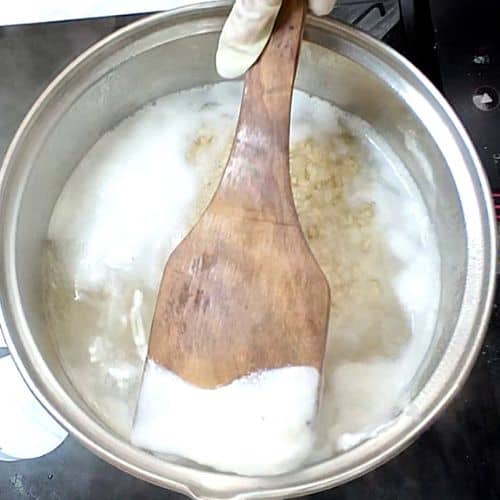Wooden spoon stirring creamy white daal mash in stainless steel pot during cooking.