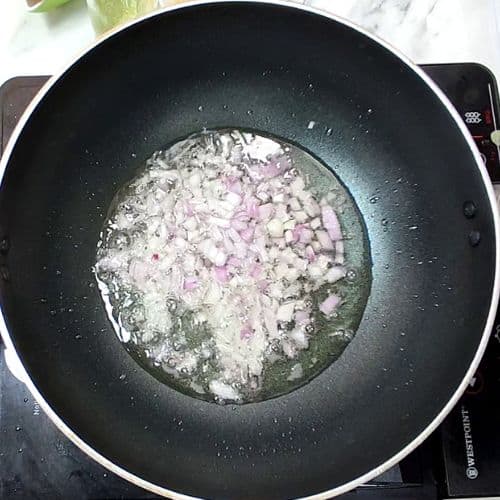 Diced onions cooking in oil in a black wok pan during Pakistani daal mash preparation.