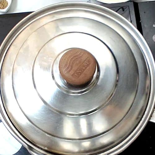 Stainless steel pot with lid containing daal mash, showing coin for size reference.