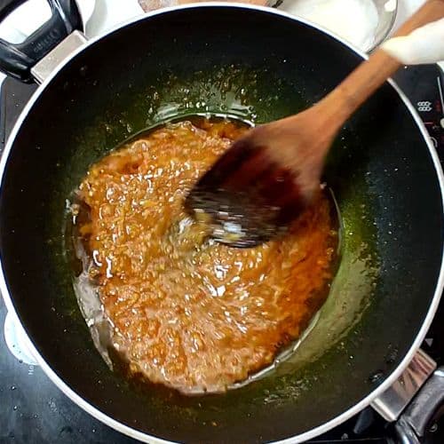 Hand stirring golden-brown daal mash in black wok with oil, Pakistani cooking preparation.
