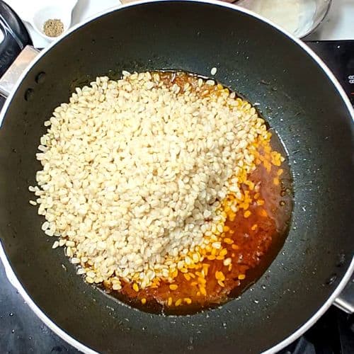 White lentils cooking in oil with spices in a dark wok for Daal Mash.