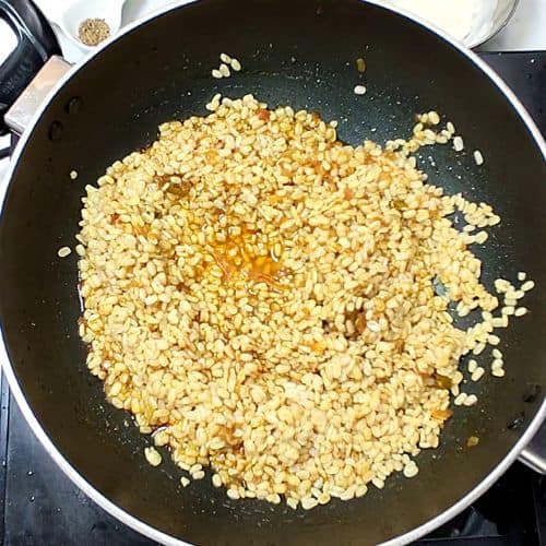Daal mash toasting in a dark pan, golden-brown lentils cooking on stovetop.