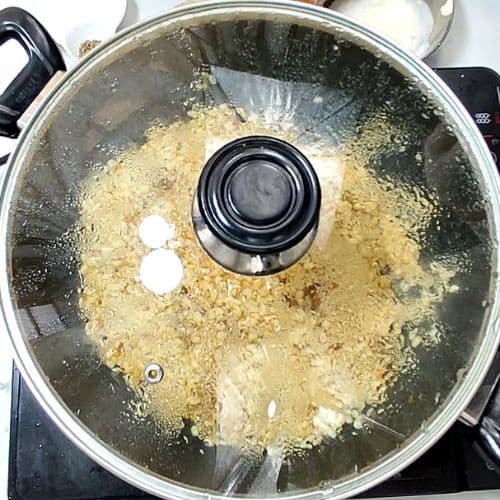 Daal mash cooking in stainless steel pot with lid, showing creamy beige-yellow cooked lentils texture.