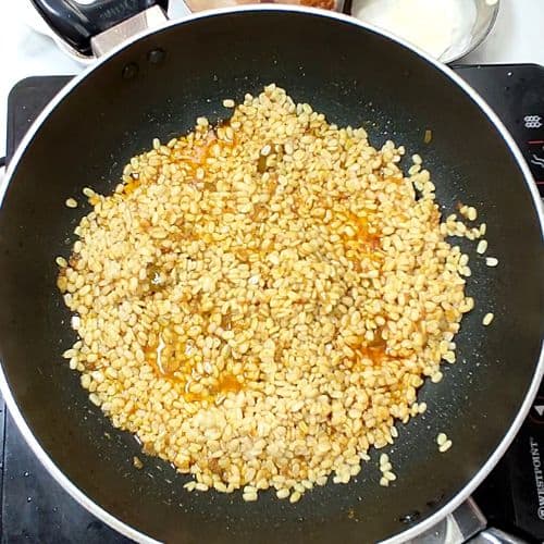 Yellow lentils being toasted in a black pan on stovetop for Daal Mash recipe.