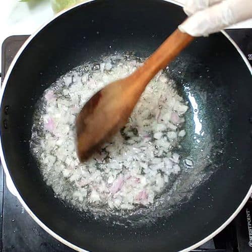Wooden spoon stirring white daal mash with onions in black wok during Pakistani cooking preparation.