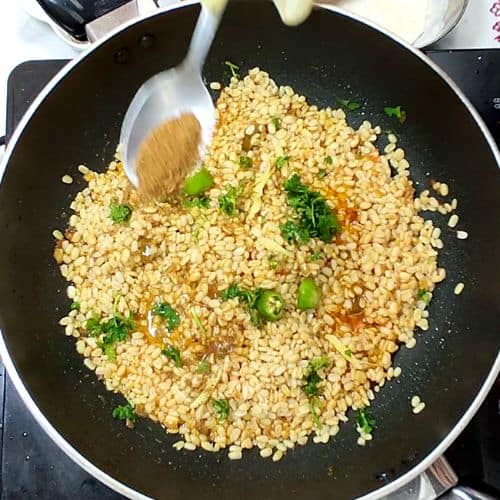 Daal Mash being stirred in a wok with green garnish and wooden spoon visible.