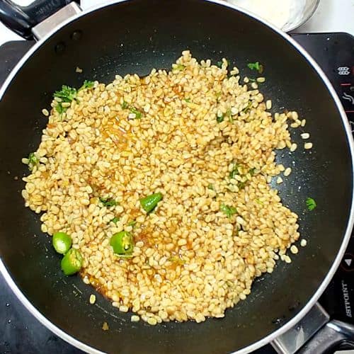 Yellow lentil daal mash cooking in a wok with green chili garnish and oil coating.