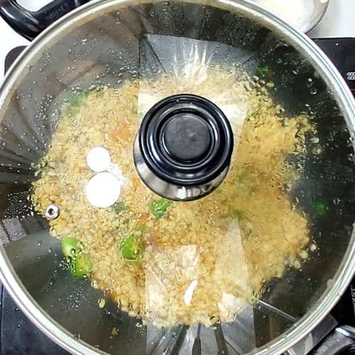 Daal mash cooking in covered pot with green onions garnish and broth visible.