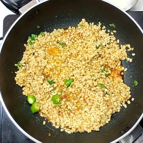 Daal Mash stir-frying in a wok with green chilies and herbs, golden-brown lentils with vibrant green garnish.