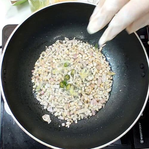 Daal mash cooking in black wok with minced meat and green onions, hands stirring with utensil.