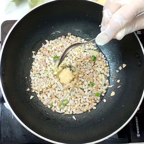 Daal mash being stirred in black wok with ginger, green herbs, and wooden spoon.